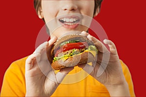 Child eats burger on red background. Male child with hamburger photo