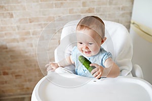 Child eats a cucumber. Appetizing vitamins . cute baby in chair. copy space