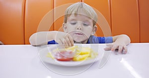 Child eats french fries with tomato sauce at table in fast food restaurant