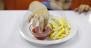 Child eats french fries with tomato sauce at table in fast food restaurant