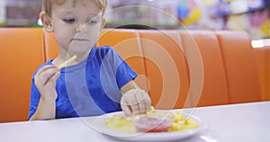 Child eats french fries with tomato sauce at table in fast food restaurant