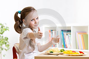 Child eats healthy food showing thumb up