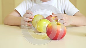 The child eats and plays with red and green apples, sits at the table. The focus of the camera moves from the face to