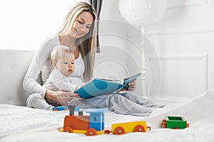 Child education. Happy mother with her toddler sitting on the bed and reading a book