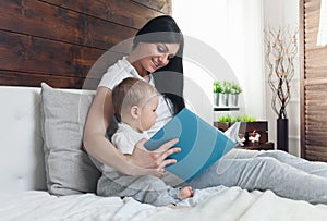 Child education. Happy mother with her toddler sitting on the bed and reading a book