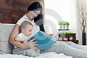 Child education. Happy mother with her toddler sitting on the bed and reading a book