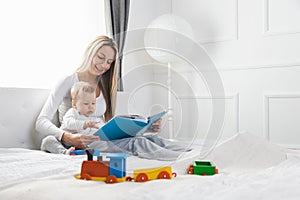 Child education. Happy mother with her toddler sitting on the bed and reading a book