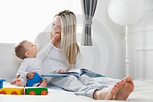 Child education. Happy mother with her toddler sitting on the bed and reading a book