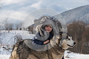 Child embraced husky dog. Boy in winter clothes with Siberian husky in snow.