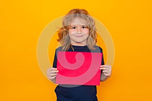 Child with empty red sheet of paper, isolated on yellow background. Portrait of a kid holding a blank placard, poster