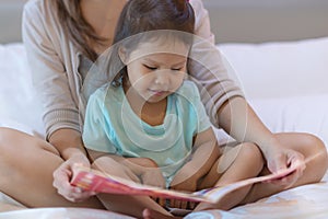 A child enjoying reading a book in bed with her mother