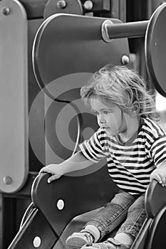 Child is entertained on a child`s swing. Cute baby boy sits on top of orange slide board