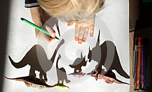 Child, with enthusiasm and concentration, outlines shadows from toy figurine of small and large dinosaurs