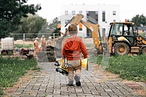 Child with excavator near construction site, dreams to be an engineer. Little builder. Education, and imagination