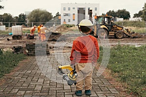 Child with excavator near construction site, dreams to be an engineer. Little builder. Education, and imagination