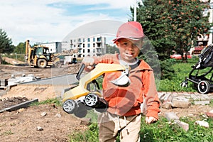 Child with excavator near construction site, dreams to be an engineer. Little builder. Education, and imagination