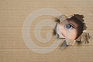 A child eye looking through a hole on a cardboard box.