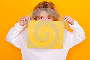 Child face close up with sheet of paper, isolated on yellow background. Portrait of a kid holding a blank placard