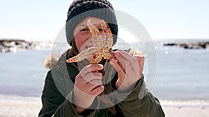 Child face, girl and starfish by beach, ocean or sea waves on summer, travel location or South Africa holiday vacation