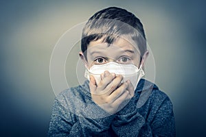 Child with face mask wraps his hands over his mouth