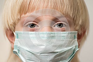 Child face in medical mask, close up. Boy is wearing disposable surgical mask