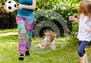 Child falling down running, playing ball with family in the garden, injury concept. Kids outdoors sport activity accident, fall