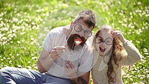 Child and father posing with eyeglases photo booth attributes at meadow. Smart and clever concept. Dad and daughter sits