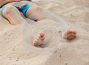 Child feet half buried in the sand on the beach