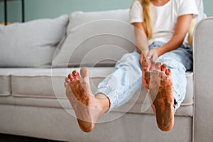A child with feet in the mud is sitting on the couch in the house
