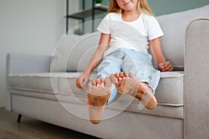 A child with feet in the mud is sitting on the couch in the house