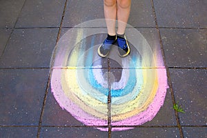 Child feet standing on chalk drawin rainbow.