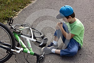 Child fell off bicycle. Boy keeps self for bruised knee