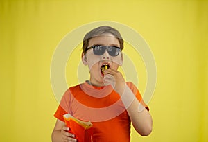 The child fills his mouth full of french fries. Isolated on a yellow background. The child eats greasy unhealthy french