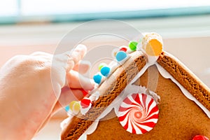 Child fingers placing candy balls and gummies on a gingerbread house roof with icing sugar as a creative and classic, seasonal