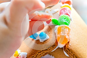 Child fingers placing candy balls and gummies on a gingerbread house roof with icing sugar as a creative and classic, seasonal