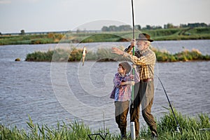 Child fishing in lake with grandfather. cath a fish with fishing rod, happy and excited