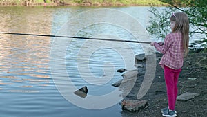 child with fishing rod is standing on the shore and fishing in the river.