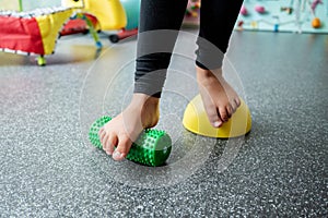 Child with flat feet standing on a spiky foot roller during kinesiotherapy