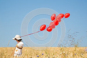 Child with flying red heart balloons on the blue sky background.