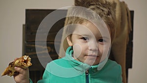 Child food concept, funny hungry kid eat pizza. Cute boy eating pizza at home. Close up face.