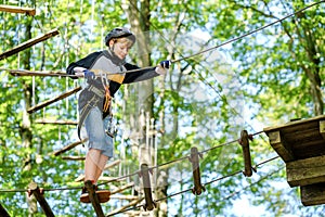 Child in forest adventure park. Kid boy in helmet climbs on high rope trail. Agility skills and climbing outdoor