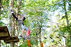 Child in forest adventure park. Kid boy in helmet climbs on high rope trail. Agility skills and climbing outdoor