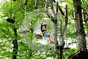 Child in forest adventure park. Kid boy in helmet climbs on high rope trail. Agility skills and climbing outdoor