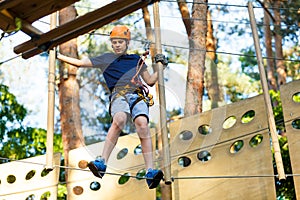 Child in forest adventure park. Kid in orange helmet and blue t shirt climbs on high rope trail. Agility skills