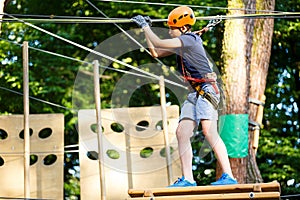 Child in forest adventure park. Kid in orange helmet and blue t shirt climbs on high rope trail. Agility skills