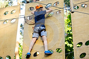 Child in forest adventure park. Kid in orange helmet and blue t shirt climbs on high rope trail. Agility skills and climbing