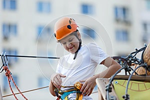 Child in forest adventure park. Kid in orange helmet and white t shirt climbs on high rope trail. Agility skills and climbing