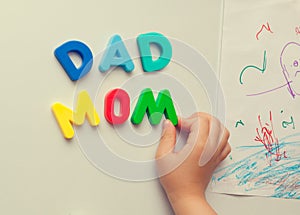 Child forms mom dad words on refrigerator