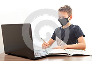 A child in front of a computer. Boy in an antibacterial mask is doing homework. Distance learning in quarantine