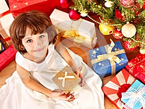 Child with gift box near Christmas tree.